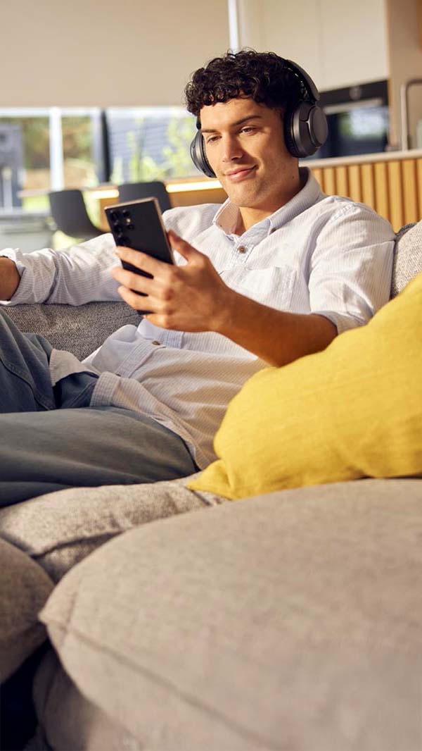 Man relaxing on a grey sofa with headphone on looking at his mobile phone
