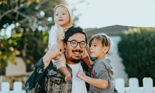A man with two children, one on his shoulder and the other to the left of him