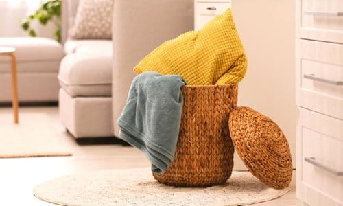 Wicker basket with yellow blanket and grey blanket stored inside