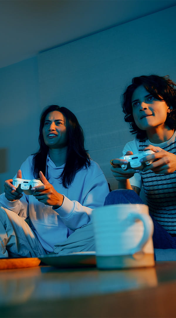 2 girls sat on a couch with computer game controllers in their hands