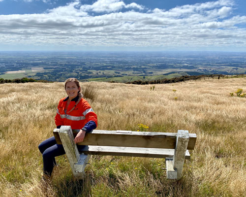 Women in high vis sitting on a bench that's on a hill with expansive views.