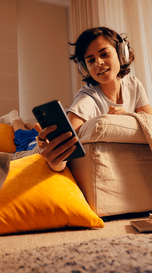 Girl on sofa using phone with headphones on