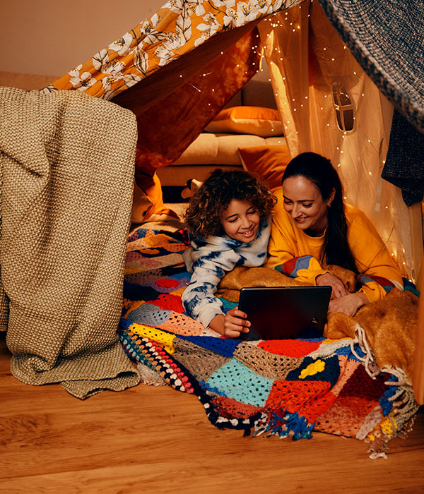 A women and her son watching a movie in a homemade fort.